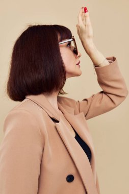 Bej ceketli, zarif güneş gözlüklü çekici bir kadın.