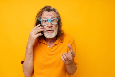 Yaşlı adam mavi gözlüklü sarı gömlekli telefonda konuşuyor.