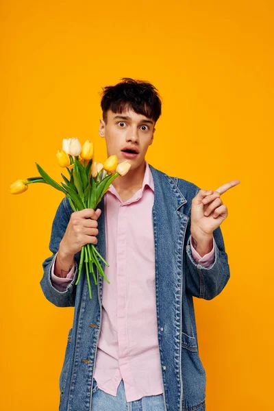 Handsome man with bouquet of flowers in denim jacket fashion yellow background — Stock fotografie