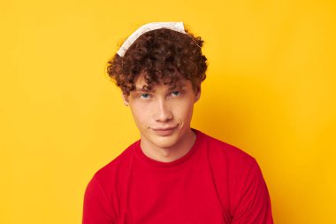 Kırmızı kıvırcık saçlı, yüzünde kırmızı t-shirt ile sarı arka plan pozu veren adam.