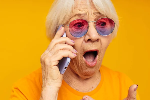 Emekli yaşlı kadının sarı gözlüklü sarı arka planda telefonla konuştuğu fotoğraf. — Stok fotoğraf