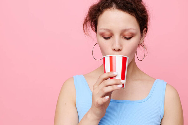cheerful girl with a disposable multi-colored glass on a pink background