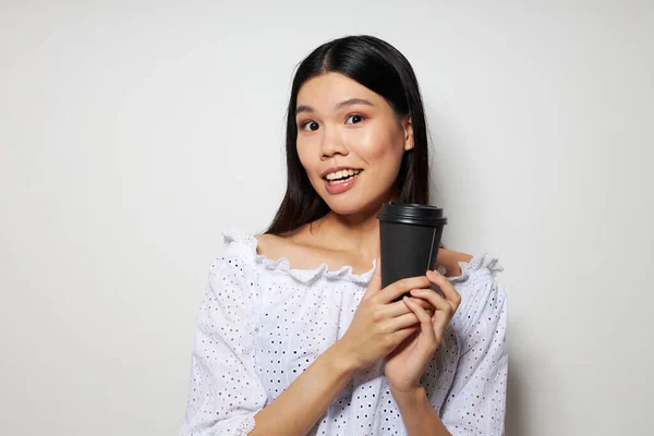 Encantadora jovem mulher asiática um copo preto nas mãos de uma bebida como um sorriso isolado fundo inalterado — Fotografia de Stock