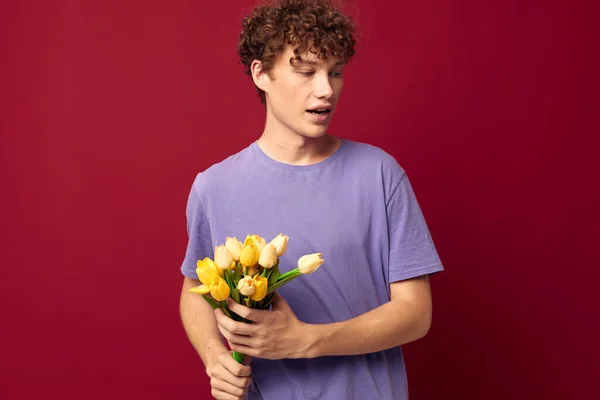 Um jovem segurando um buquê amarelo de flores camisetas roxas fundo vermelho inalterado — Fotografia de Stock