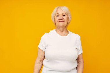 Elleri sarı arka planda, sıradan tişörtlü yaşlı bir kadın.