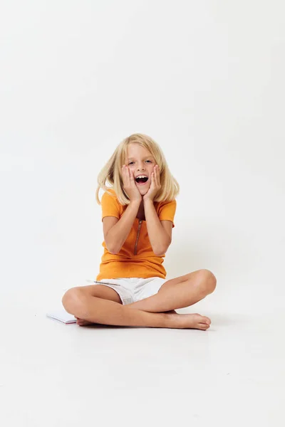 Ein fröhliches kleines Mädchen in einem gelben T-Shirt sitzt mit gefalteten Beinen auf dem Boden — Stockfoto