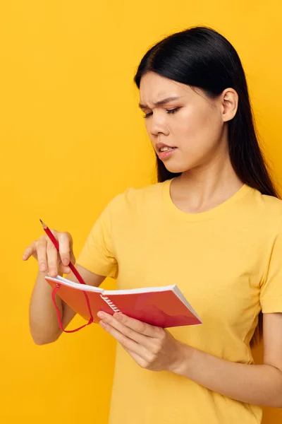 Femme avec l'apparence asiatique dans un t-shirt jaune carnet rouge formation fond jaune inchangé — Photo