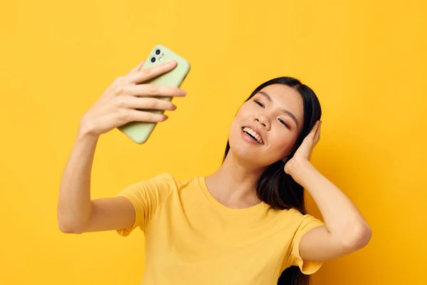 휴대폰 포즈 스튜디오 모델을 보고 있는 노란 티셔츠를 입고 있는 여성 — 스톡 사진