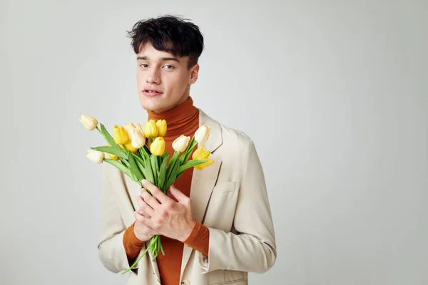 黄色の花の花束を持つ白いジャケットの美しい男エレガントなスタイルのモデルスタジオ — ストック写真
