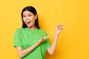 Asyalı, yeşil tişörtlü güzel bir kadının portresi elleri ve duyguları değişmeden sarı arka planda.