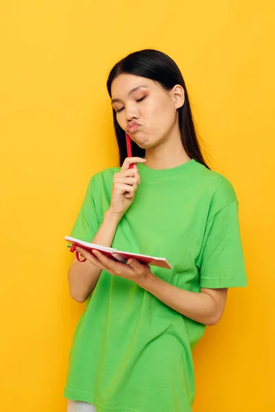 Femme avec apparence asiatique T-shirts verts avec carnet rouge et stylo fond jaune inchangé — Photo