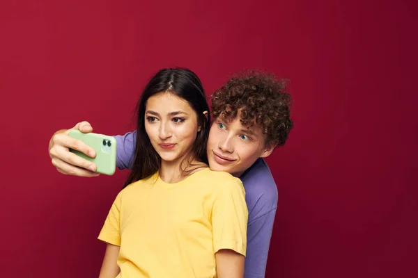 Een jong koppel in kleurrijke T-shirts met een telefoon geïsoleerde achtergrond — Stockfoto
