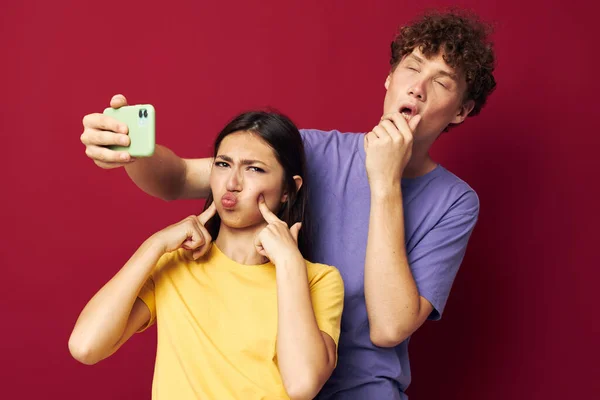 Gentil gars et fille dans coloré T-shirts avec un téléphone fond rouge — Photo
