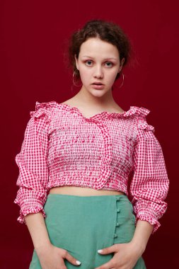 Pembe tişörtlü hoş bir kız. El kol hareketleri yapıyor. Stüdyo kırmızı arka plan.