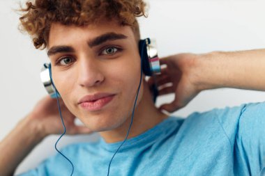 Mavi tişörtlü çekici bir adam kulaklık giyer, izole edilmiş arka plan.