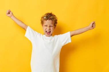 Beyaz tişörtlü kıvırcık çocuk. Gözlüklü, el kol hareketi yapıyor. Arka planda bir değişiklik yok.