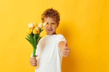 Sevimli küçük çocuk elinde bir buket çiçek, sarı bir arkaplan, değiştirilmemiş.