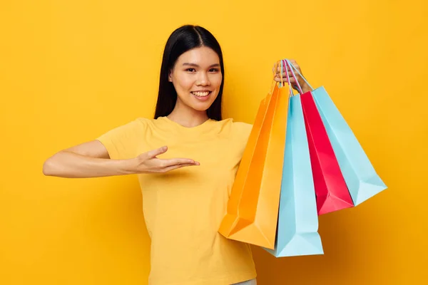 Pretty brunette in a yellow T-shirt with multicolored shopping bags yellow background unaltered — Stockfoto