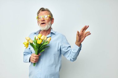 Yaşlı adam bir buket çiçek ve hediye olarak hafif bir arka plan.