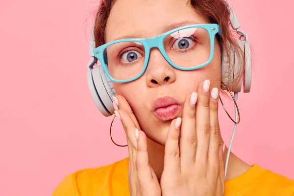 Jolie fille portant des lunettes bleues écoutant de la musique sur fond rose casque inchangé — Photo