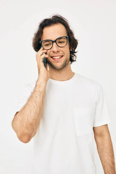 Bonito homem em um branco t-shirt comunicação por telefone luz fundo — Fotografia de Stock