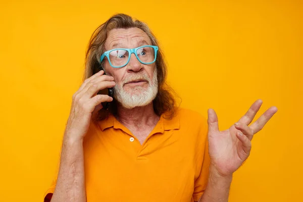 Vieil homme en T-shirts jaunes et lunettes parlant au téléphone fond isolé — Photo