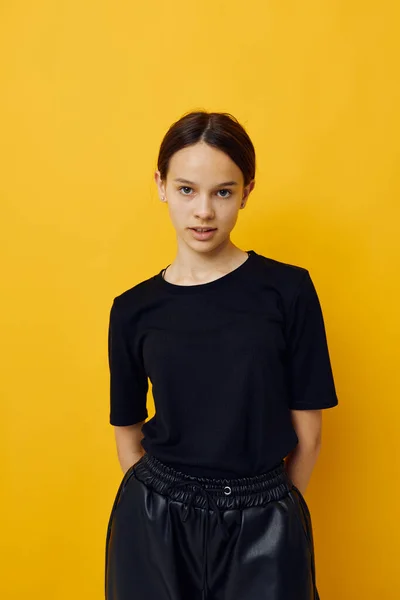 Menina bonita em uma camiseta preta e calças sorrir fundo amarelo — Fotografia de Stock