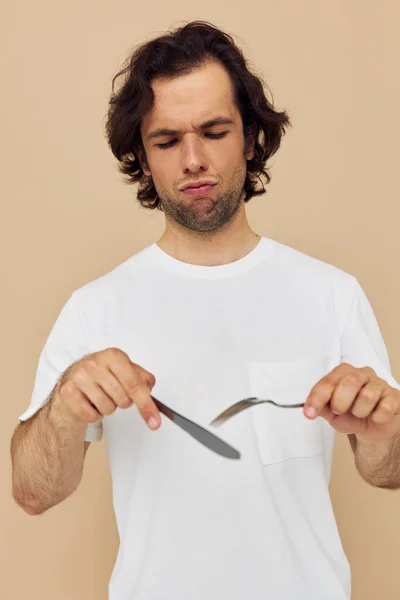 Aantrekkelijke man in een wit T-shirt met mes met vork geïsoleerde achtergrond — Stockfoto