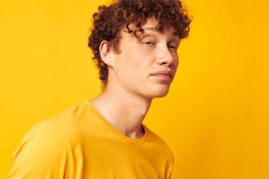Kırmızı kıvırcık saçlı, şık gözlüklü, sarı tişörtlü, izole edilmiş arka plan pozu veren adam.