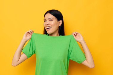 Asyalı, yeşil tişörtlü güzel bir kadının portresi. Elleriyle jestler yapıyor. Duyguları değişmemiş.