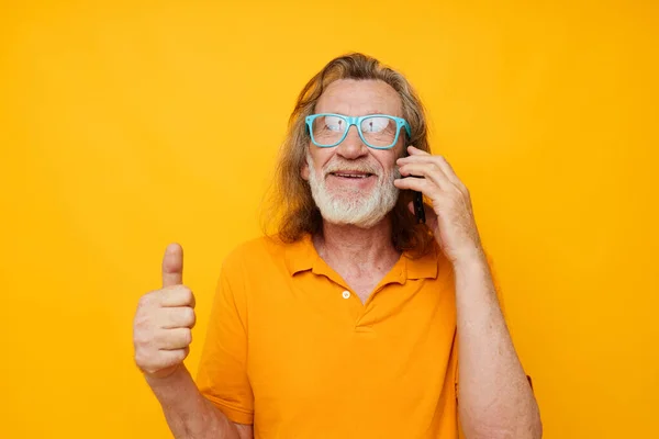 Homme âgé aux cheveux gris portant des lunettes bleues chemise jaune parlant au téléphone fond isolé — Photo