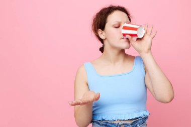 Güzel kız cam bir içecekten içiyor. Pembe arka plan, değişmeden yakın plan.