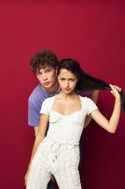 Bir adam bir kızın arkasında durur ve saçlarını kırmızı arka planda tutar.