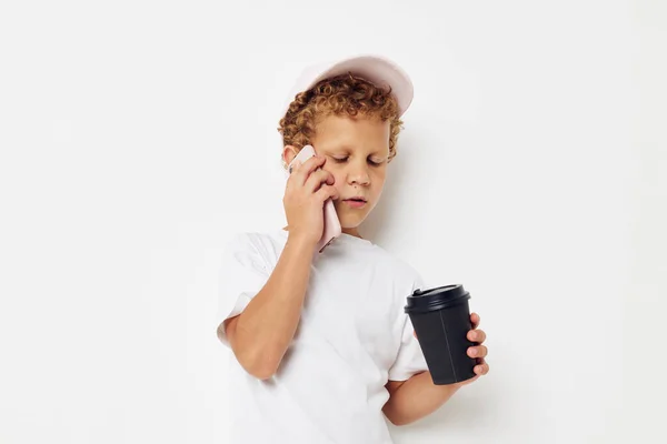 Lindo chico en una gorra de camiseta blanca con un teléfono en un vaso con un estilo de vida de bebida inalterado — Foto de Stock