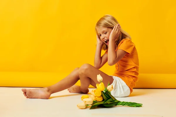 Bir buket çiçekle yerde oturan küçük kız sarı arka planda — Stok fotoğraf