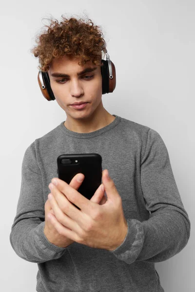 Homem atraente com um telefone na mão ouvindo música em fones de ouvido fundo de luz — Fotografia de Stock