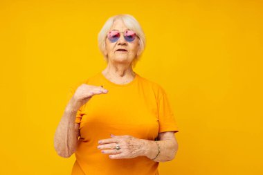 Gündelik tişörtlü, güneş gözlüklü yaşlı bir kadın izole edilmiş arka plan