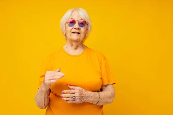 Smiling elderly woman in a yellow t-shirt posing yellow background — ストック写真
