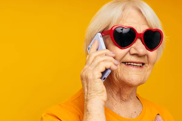 Портрет старой дружелюбной женщины в темных очках, разговаривающей по телефону на изолированном фоне — стоковое фото