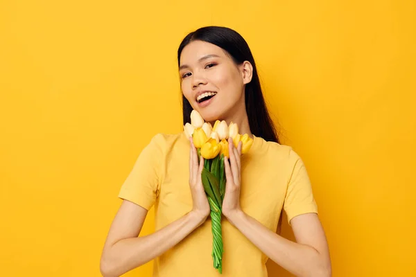 손에 꽃다발을 들고 아시아의 모습을 하고 있는 여자는 아무런 변화 없이 노란 배경을 그리며 즐거움을 선사한다 — 스톡 사진