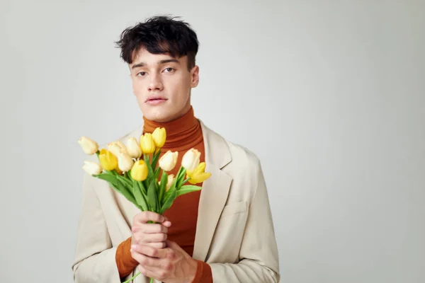 Ένας νεαρός άνδρας με λευκό σακάκι με ένα μπουκέτο κίτρινα λουλούδια κομψό στυλ φόντο αναλλοίωτο — Φωτογραφία Αρχείου