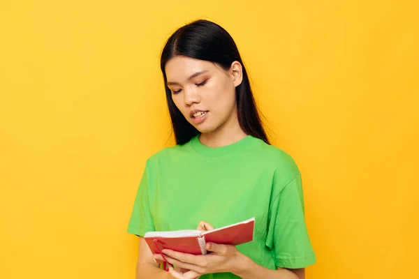 लाल नोटबुक आणि पेन पिवळा पार्श्वभूमीसह सुंदर श्यामला हिरवा टी-शर्ट अनियंत्रित — स्टॉक फोटो, इमेज