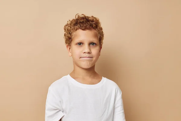 Veselý chlapec s kudrnatými vlasy v bílém tričku béžové pozadí — Stock fotografie