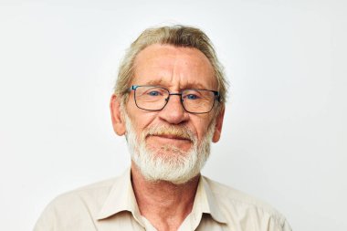 Gri sakallı, gömlekli ve gözlüklü, açık renk arka planlı yaşlı bir adam.