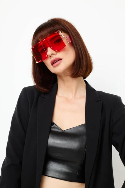 Mujer atractiva en rojo con gafas con estilo un traje de cuero chaqueta negra fondo claro — Foto de Stock