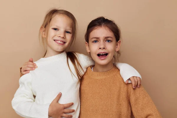 Две забавные маленькие девочки обнимают дружбу, представляя бежевый фон — стоковое фото