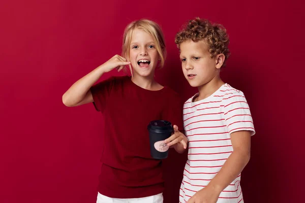 Мальчик и девочка стоят рядом с одноразовым стаканом на красном фоне — стоковое фото