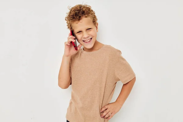Cute boy with curly hair holding a red phone light background — Stock fotografie