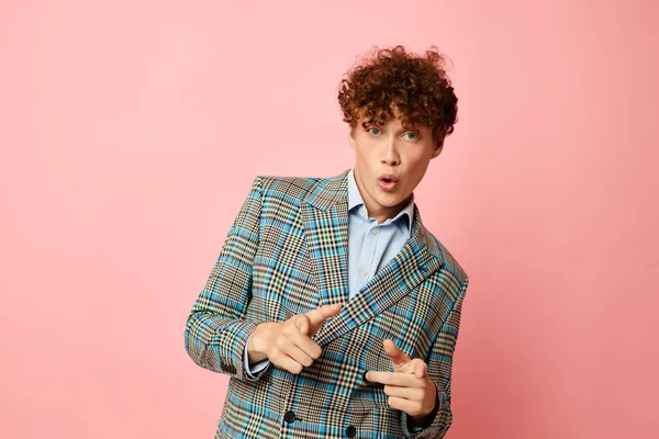 Portrait of a young curly man checkered blazer elegant style posing fashion pink background unaltered Foto Stock