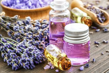 Ahşap bir masanın üzerinde kurutulmuş lavanta çiçekleri olan lavanta spa ürünleri. Tahta zemine banyo tuzu ve masaj yağı serpiştirilmiş. Cilt bakımı, güzellik tedavi konsepti. Lavendula oleum